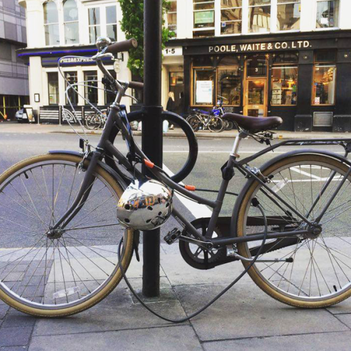 Black bike and silver helmet locked up and parked in a Cyclehoop bike stand on a city street